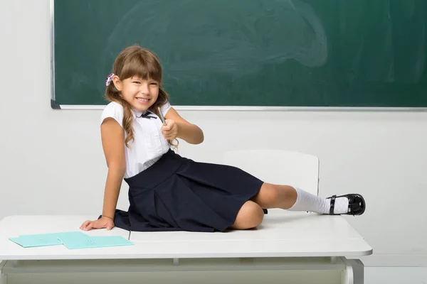 Glückliches Schulmädchen sitzt auf Schreibtisch im Klassenzimmer — Stockfoto