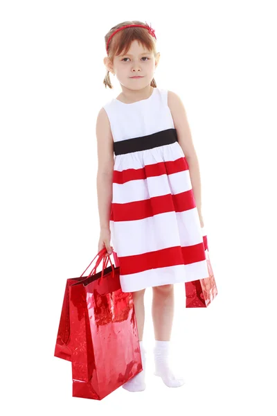Menina em um vestido listrado segurando pacotes vermelhos — Fotografia de Stock