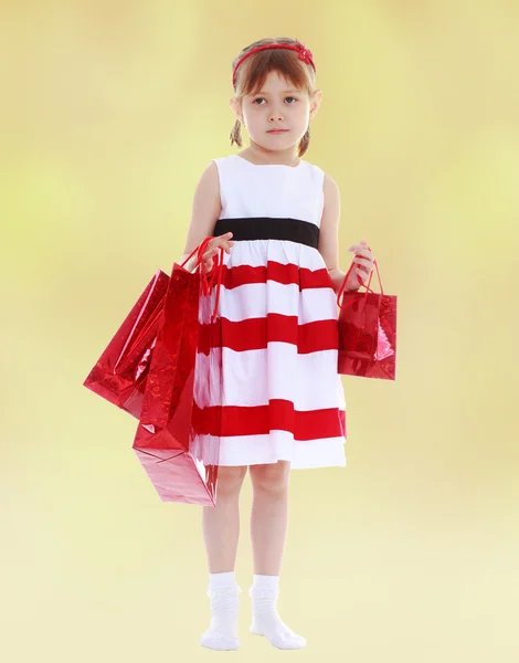 Menina em um vestido listrado segurando sacos de compras de papel vermelho . — Fotografia de Stock