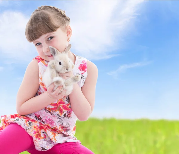 Little girl holding a rabbit sitting on meadow. — Stock Photo, Image