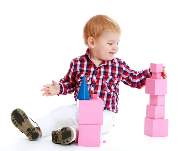 Little boy collects pink pyramid. — Stock Photo, Image