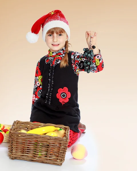 Little girl in santa claus hat holding a bunch of grapes. — Stock Photo, Image