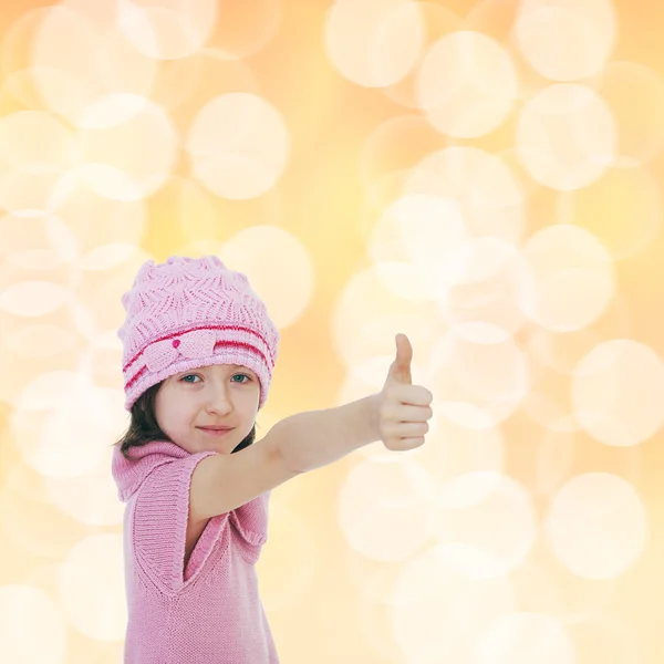 Malá holčička, pletené čepice ukazuje palec. — Stock fotografie