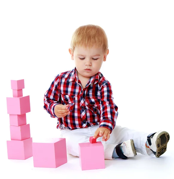 Little boy collects pink pyramid. — Stock Photo, Image