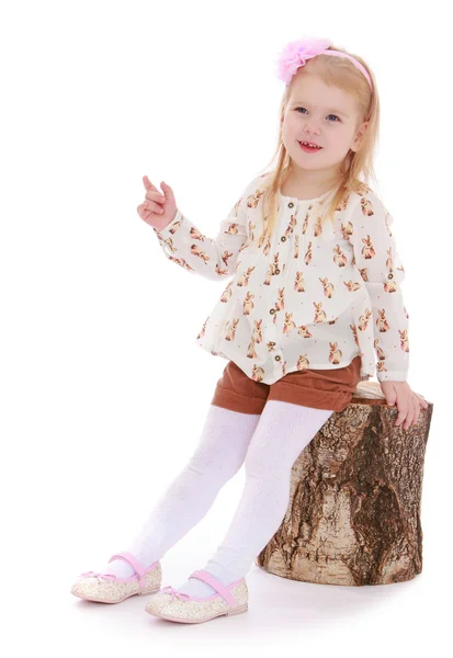 Little girl in shorts sitting on a stump on. — Stock Photo, Image