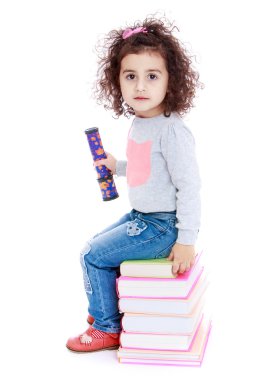 küçük kız mavi jeans bir yığın kitap üzerinde oturuyor.