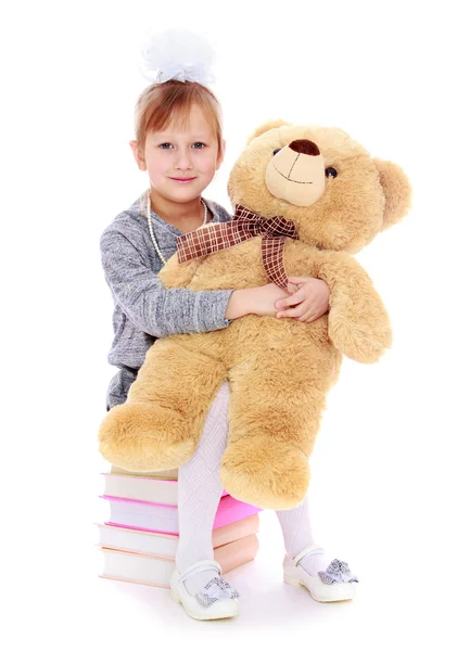 Adorable little girl sitting on books and holding a big teddy be — Stock Photo, Image