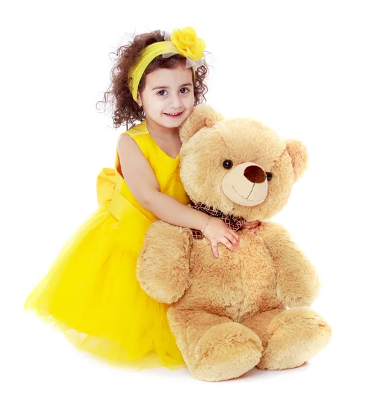 Büyük ayıcık sarılmayı sarı elbiseli sevimli küçük kız. — Stok fotoğraf