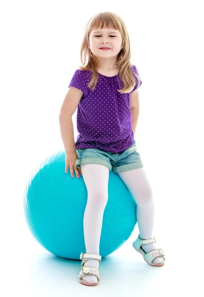 Little girl in short sports shorts sitting on the big blue. — Stock Photo, Image