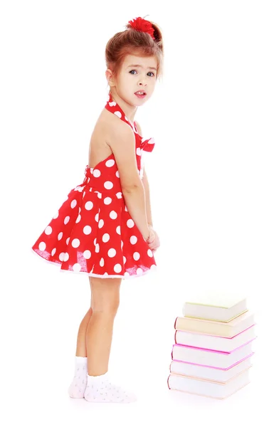 Adorable little girl in a short red dress standing next to a boo — Stock Photo, Image