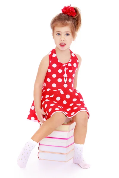 Encantadora niña con un vestido rojo sentado en los libros . — Foto de Stock