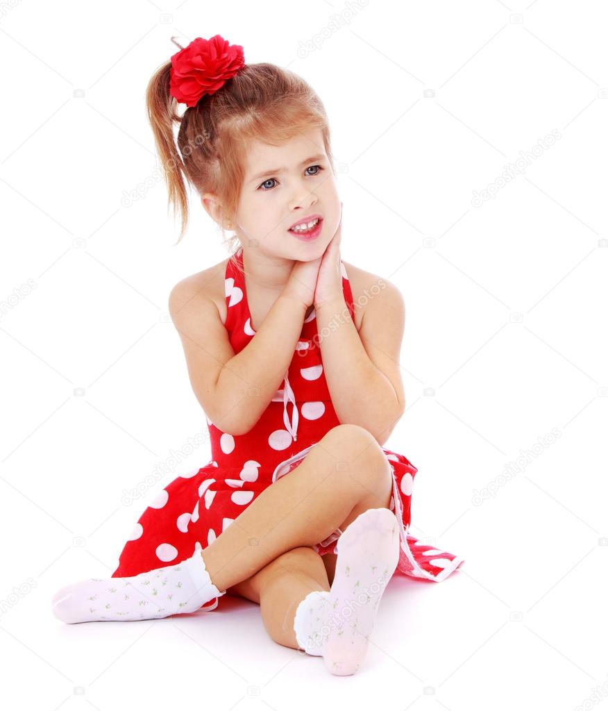 Beautiful little girl sitting on the floor crossed her legs.