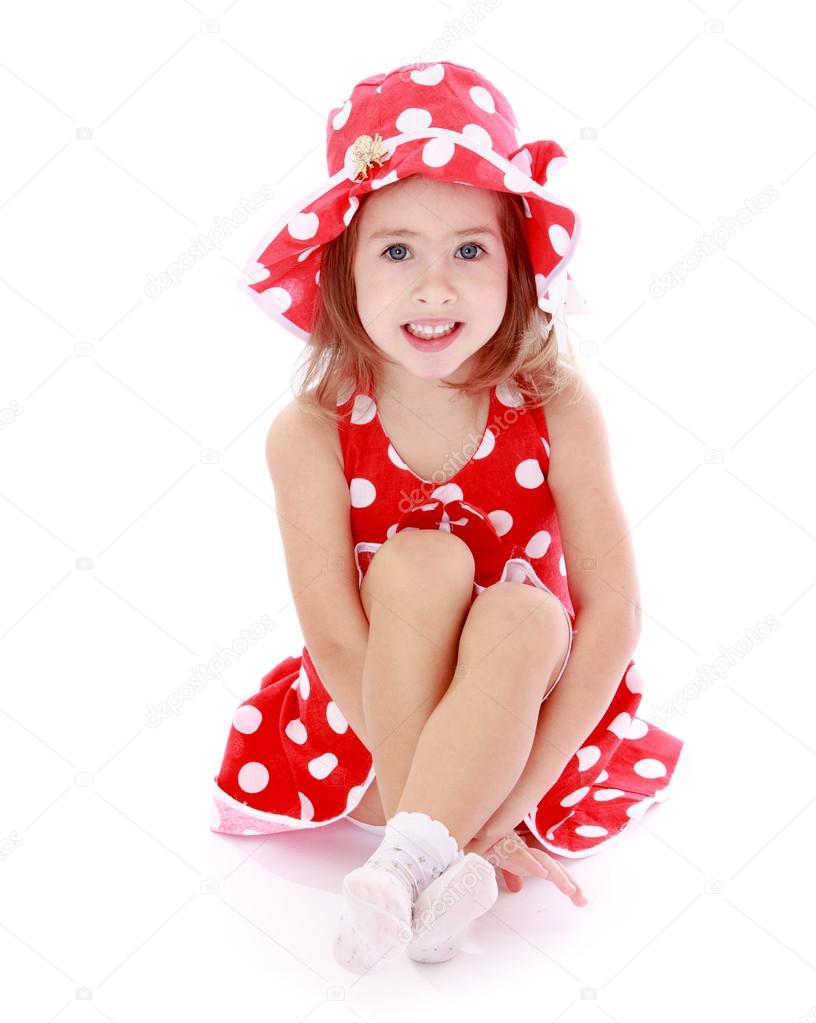 beautiful little girl in a red polka-dot dress sitting on the fl