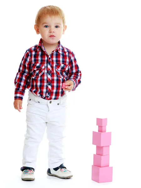 Little boy collects pink pyramid. — Stock Photo, Image