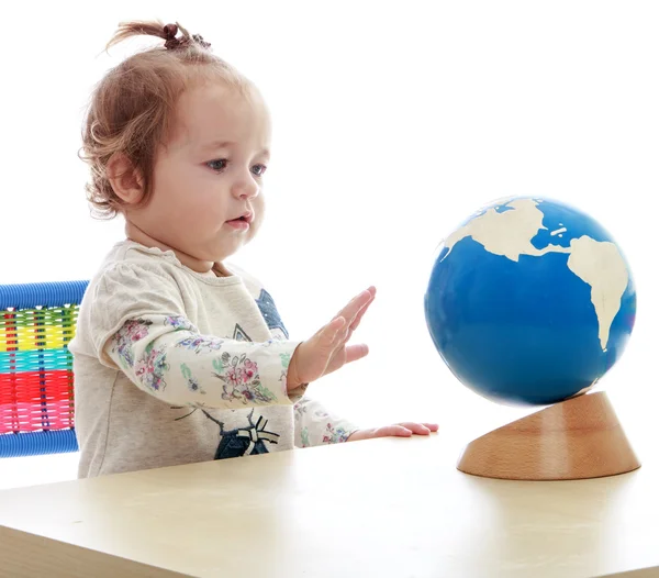 Velmi malé, ale vážné holčička točí zeměkoule ruka. — Stock fotografie