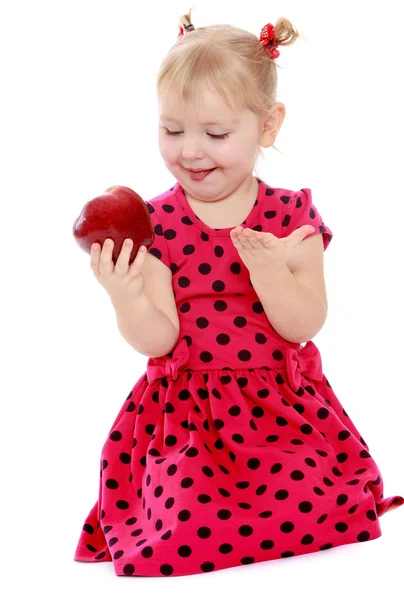 Funny little girl looks at a delicious red apple. — Stock Photo, Image