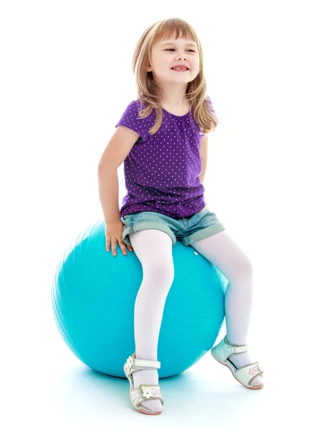 Kleines Mädchen in kurzen Shorts sitzt auf dem großen blauen Leinen. — Stockfoto