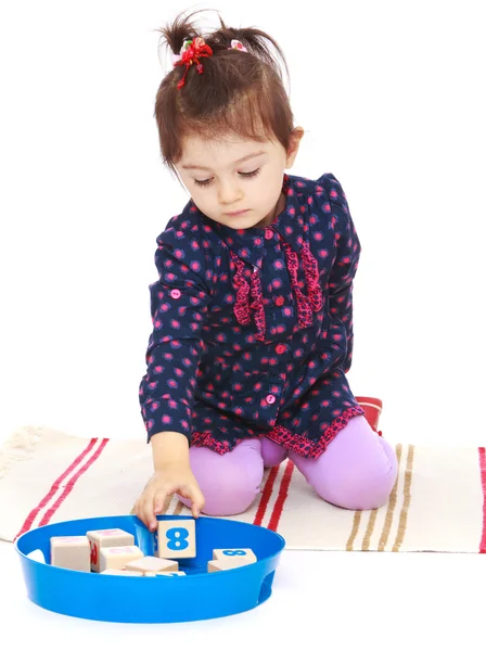 Schattig klein meisje zet kubussen zittend op de vloer. — Stockfoto
