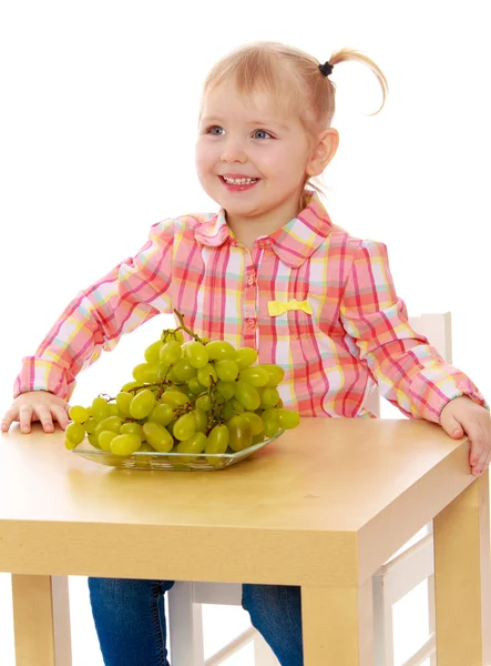 Hermosa chica caucásica comiendo uvas sentada en la mesa . —  Fotos de Stock