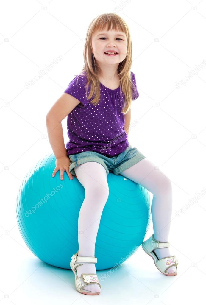 Very cute little girl sitting on a big ball sports.