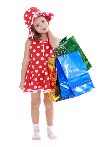 Smiling girl in a summer dress and hat holding a multi-colored b — Stock Photo, Image