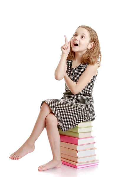 Fröhliches Mädchen sitzt auf den Büchern und zeigt den Daumen nach oben — Stockfoto