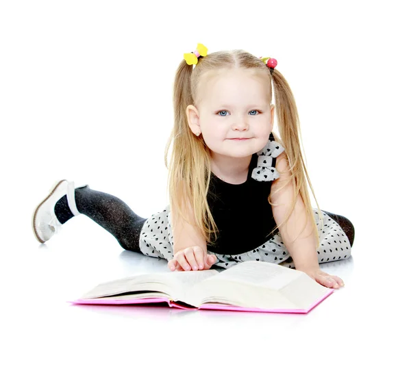 Bedårande liten flicka med flätor läser en bok. — Stockfoto