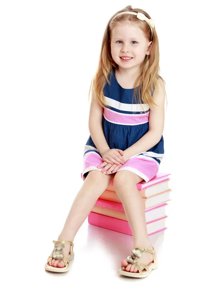 Adorable niña sentada en una pila de libros . — Foto de Stock