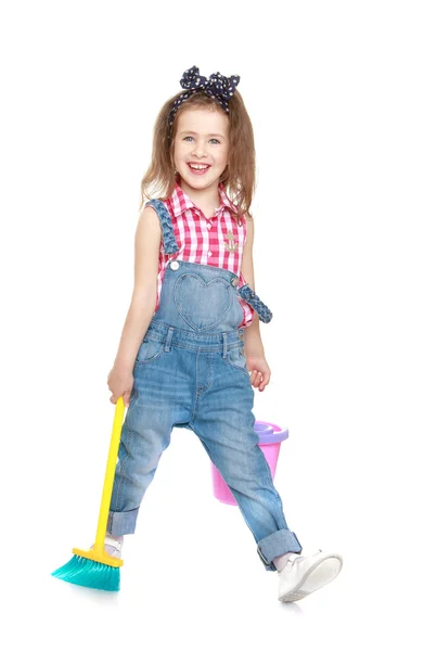 Funny little girl in denim overalls sweeping the floor Stock Picture