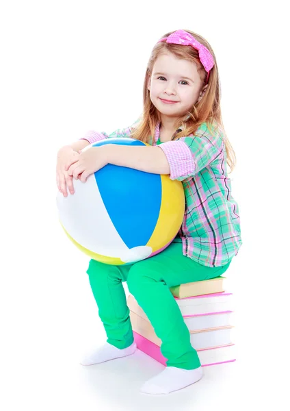 Little girl sitting on a stack of books and holding an inflatabl — Stock Photo, Image