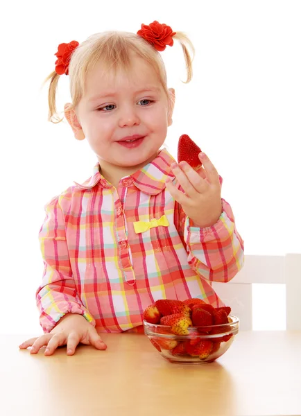 可爱的小女孩抱着一颗草莓，坐在桌前 — 图库照片