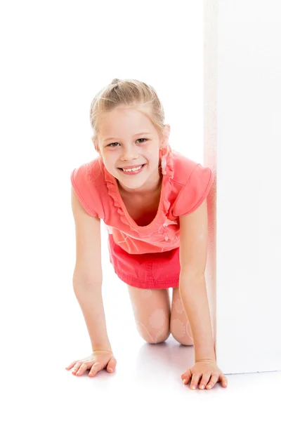 Sonriente chica mira hacia fuera desde detrás de una pared blanca — Foto de Stock