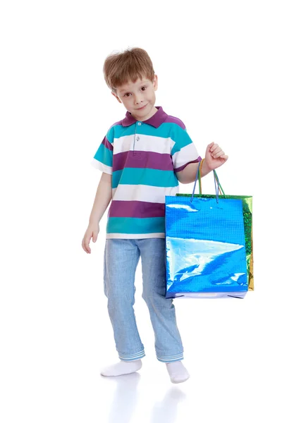 Lille pojken i randig t-shirt och jeans hålla shoppingkassar — Stockfoto
