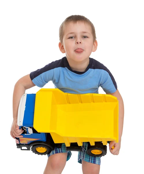 Funny little boy showing tongue holding a large toy car — Stock Photo, Image