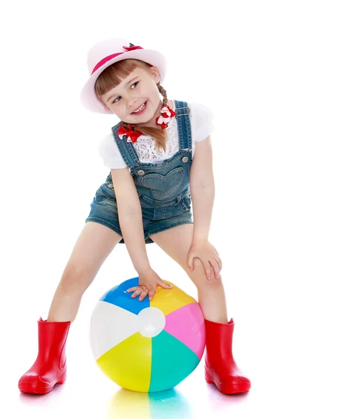 Chica alegre en pantalones cortos, sombrero y botas de goma jugando pelota —  Fotos de Stock