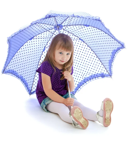 Menina senta-se no chão sob um grande guarda-chuva azul — Fotografia de Stock