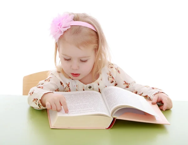 Very smart little girl reading a thick book sitting on the table — Stock Photo, Image