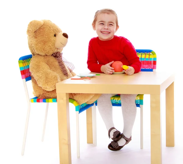 Muchacha divertida jugando con el oso de peluche sentado a la mesa — Foto de Stock