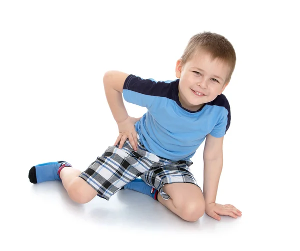 Kleine jongen in een blauw shirt en geruite broek zittend op de vloer — Stockfoto