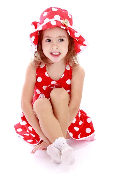 Adorable little girl in a red dress and hat with polka dots sitt — Stock Photo, Image