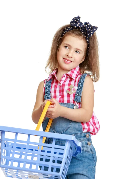 Beautiful, stylish little girl in denim overalls holding a shopping basket — Stock Photo, Image