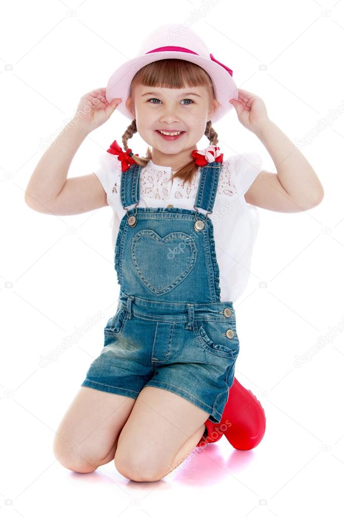 Adorable little girl in denim overalls and a hat