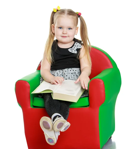 Blonde little girl reading a book sitting on the chair — Stock Photo, Image
