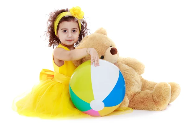 Красива елегантна дівчина в жовтій модній сукні з м'ячем і плюшевим ведмедем — стокове фото