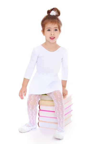 Bella bambina con un vestito bianco è seduta sui libri — Foto Stock
