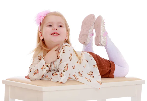 Портрет лежащий на скамейке и улыбающаяся маленькая девочка в белом. — стоковое фото