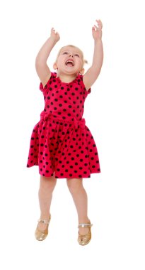 Blonde little girl in a red polka dot dress jumps his arms raise