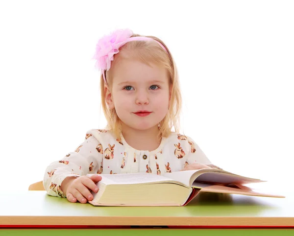 The little blonde girl with bow on her head is reading a thick b — 图库照片