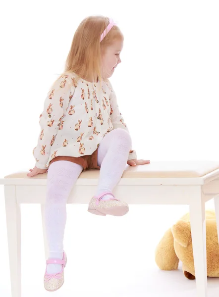 Beautiful little blonde girl in shorts and a white top sitting o — Stock Photo, Image