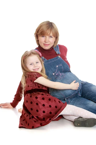 Happy little blonde girl in a long brown dress with polka dots hand stroking the belly of his beloved pregnant mom — Stock Photo, Image